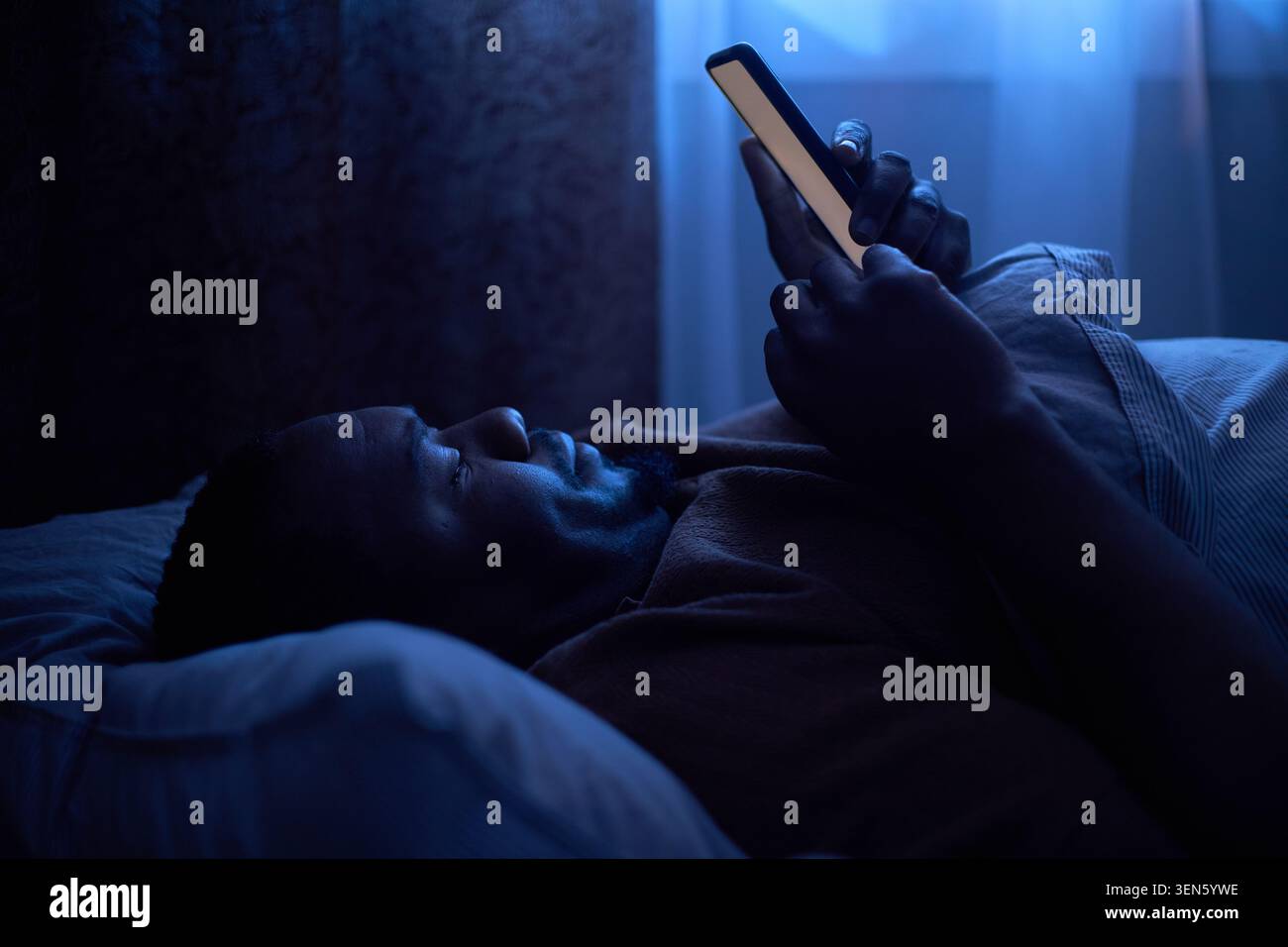 Noir homme adulte naviguant smartphone dans le lit pour la perturbation du sommeil Banque D'Images