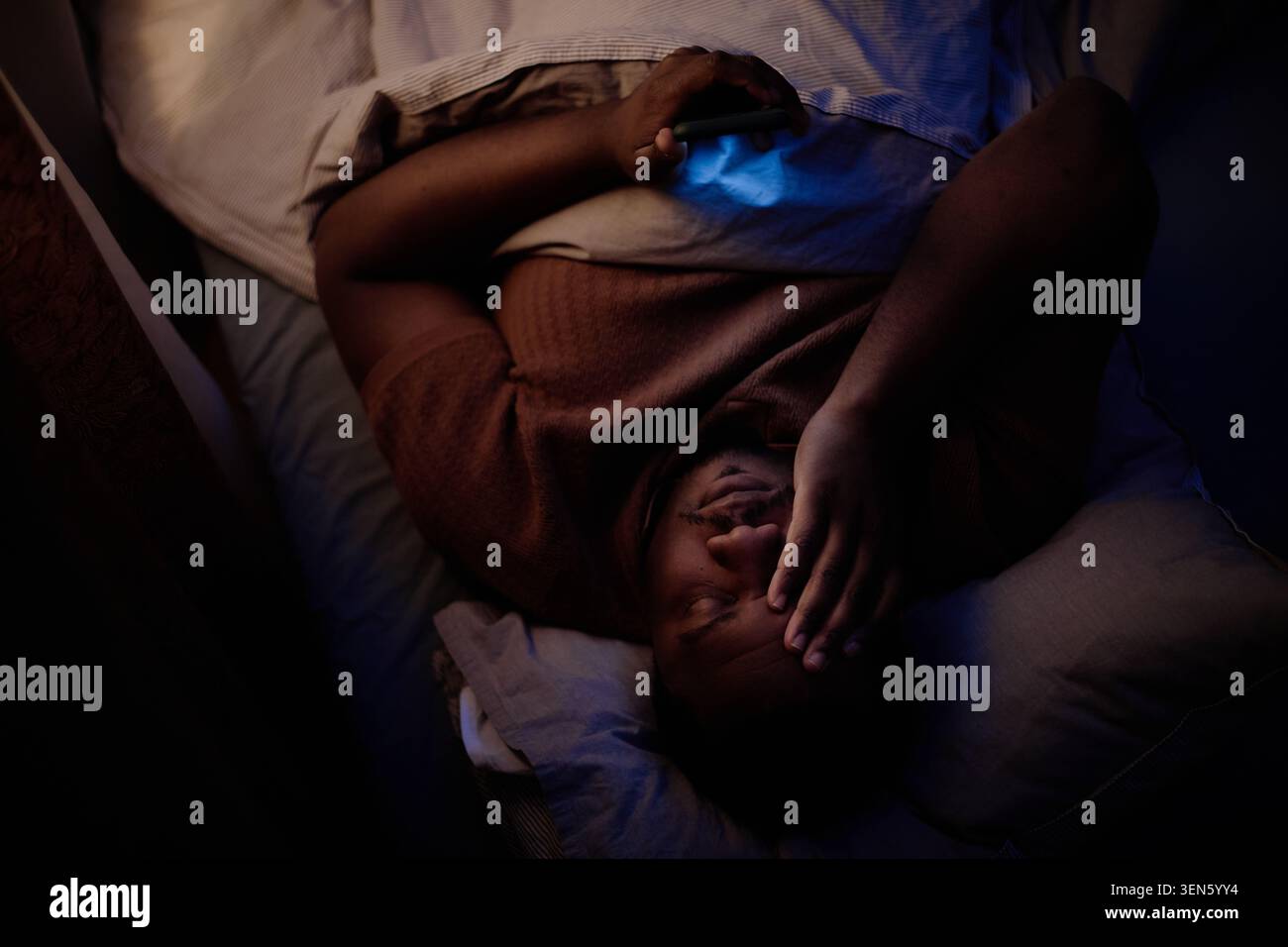 Homme noir reposant dans le lit avec smartphone pendant le stress de l'écran de nuit Banque D'Images