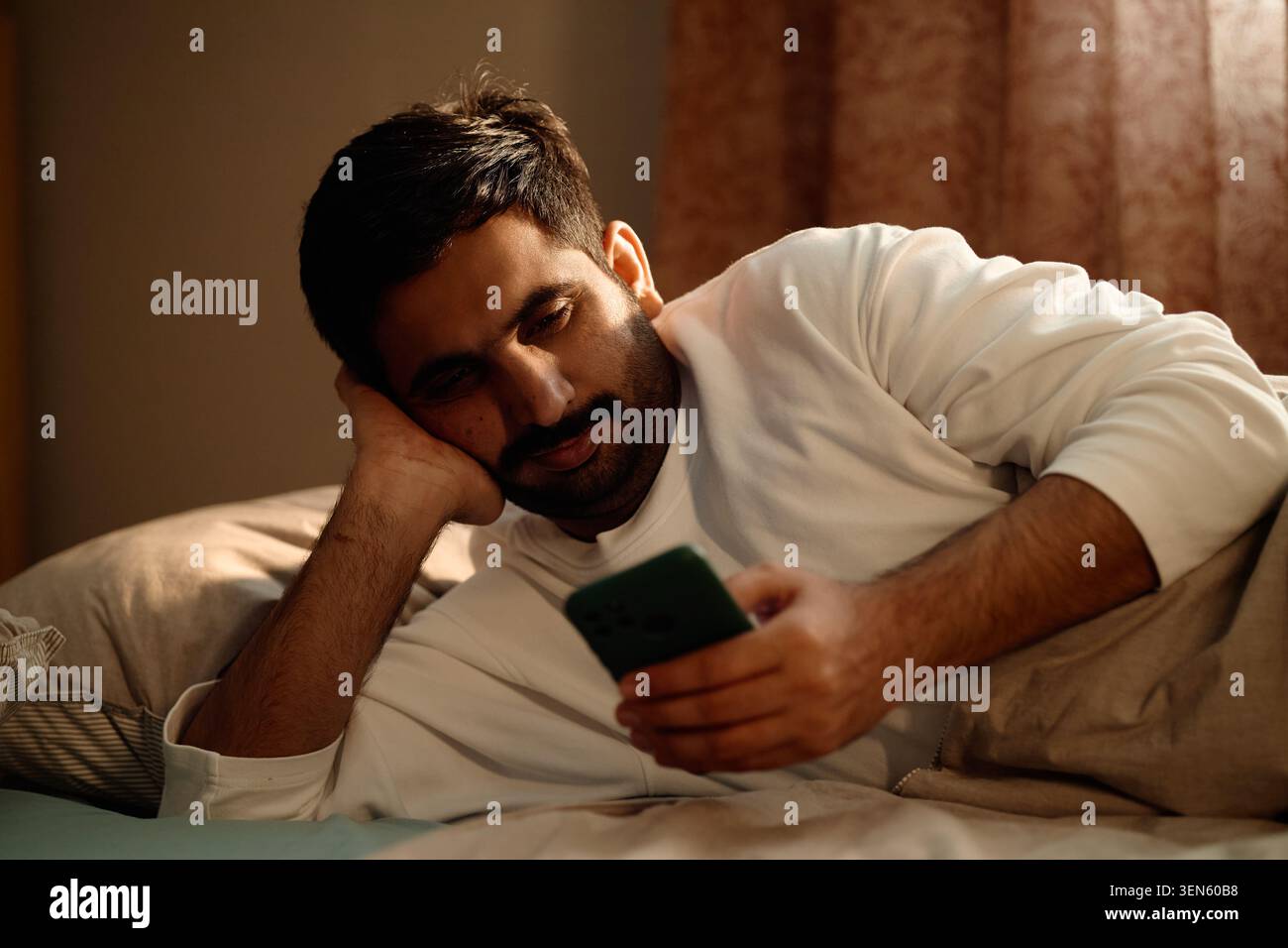 Homme adulte utilisant un smartphone dans le lit montrant la fatigue numérique à la maison Banque D'Images