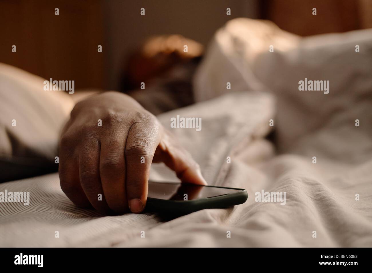 Homme noir atteignant pour smartphone dans le lit pour la dépendance de temps d'écran Banque D'Images