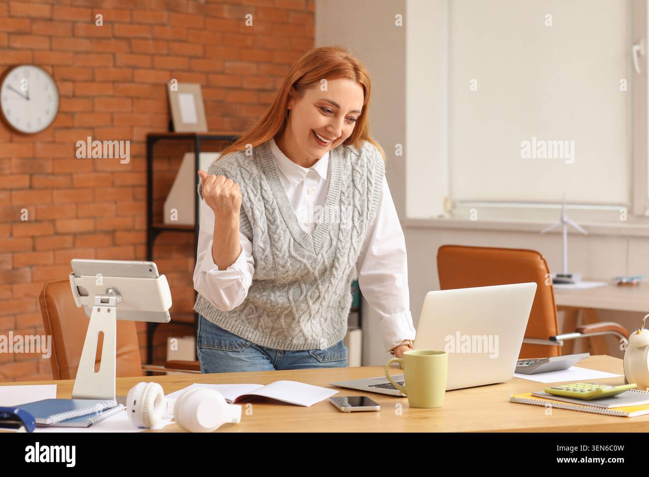 Femme d'affaires excitée célébrant le succès au bureau moderne avec ordinateur portable et tablette, atteignant des objectifs et la croissance financière Banque D'Images
