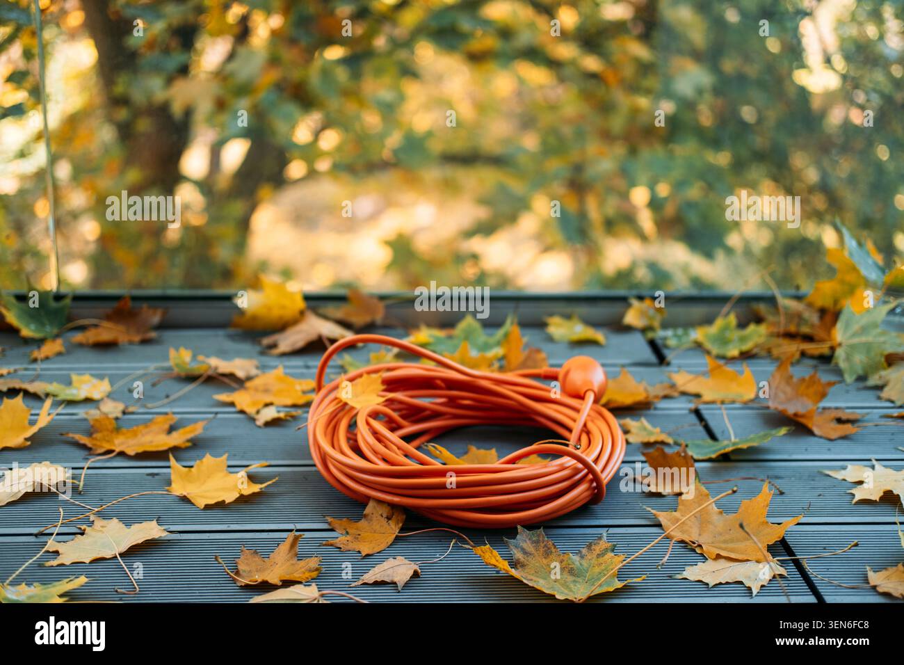 cordon d'extension enroulé orange repose sur une terrasse en bois nervurée grise à côté de feuilles d'érable jaunes éparpillées d'automne. Isolation de câble extérieur, étanche Banque D'Images