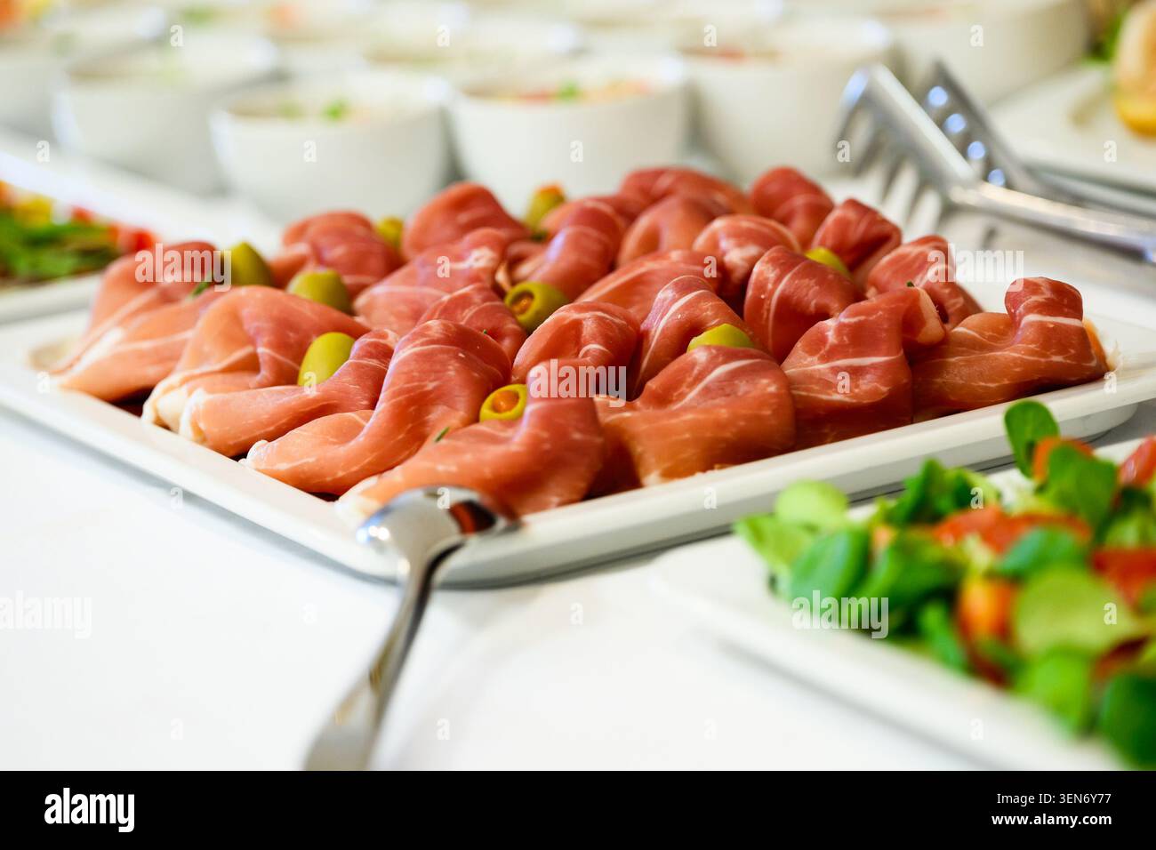 Un plat de buffet magnifiquement arrangé avec des plis élégants de prosciutto haut de gamme associés à des olives vertes éclatantes. Le gros plan met en évidence le Banque D'Images