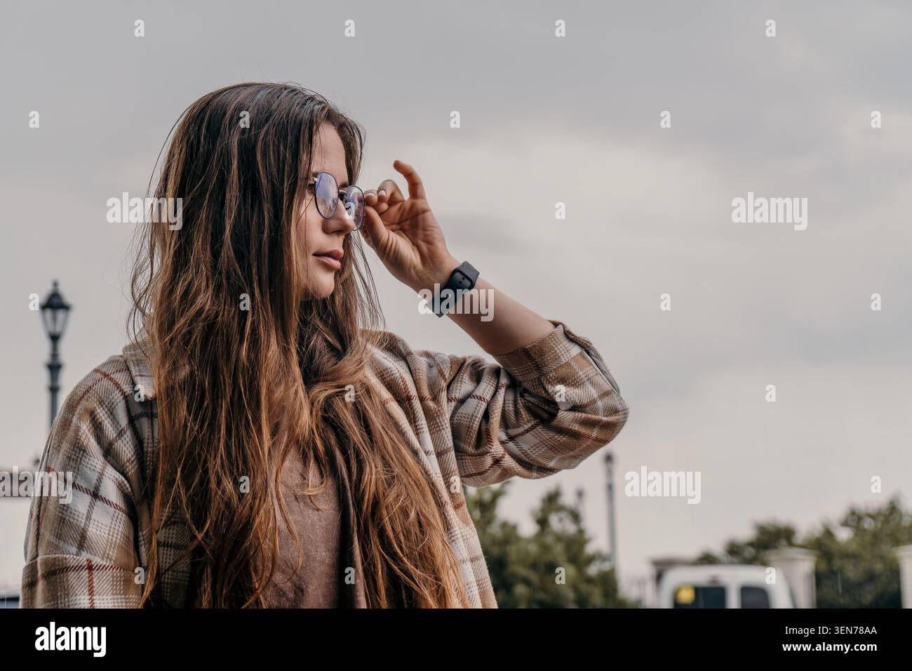 Lunettes femme extérieur regardant de côté touchant le cadre des lunettes lors d'une promenade sur une journée nuageuse avec espace de copie Banque D'Images