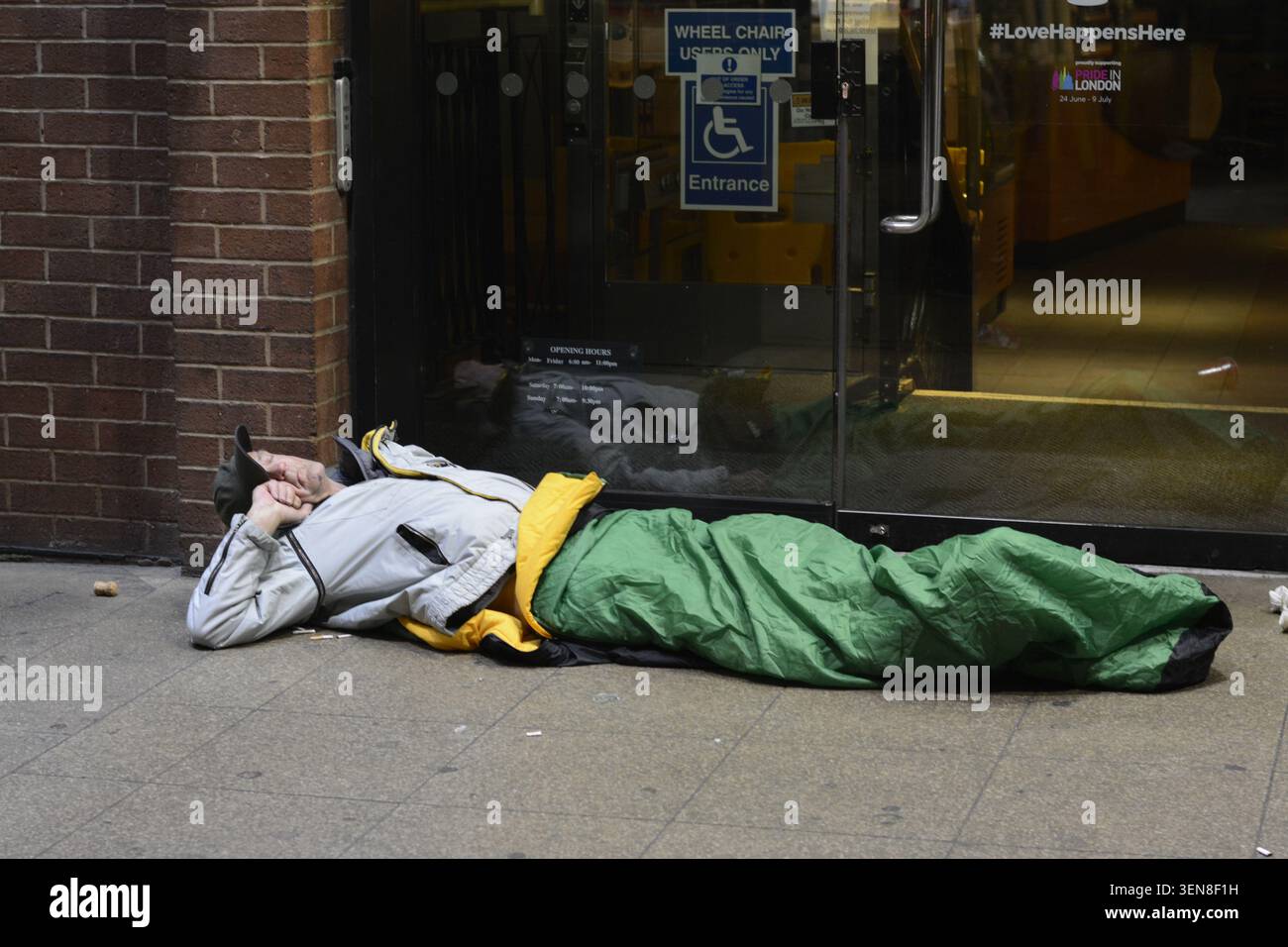 Un sans-abri dort dans une porte dans une rue urbaine du Royaume-Uni, enveloppé dans la literie à côté d'un panneau d'accessibilité, soulignant le sommeil difficile Banque D'Images