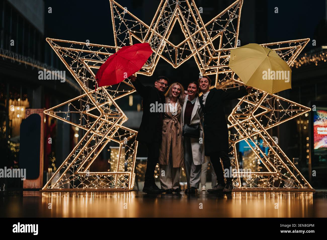 Amis et collègues d'affaires célébrant sous les lumières de Noël avec des parapluies dans la nuit de la ville Banque D'Images