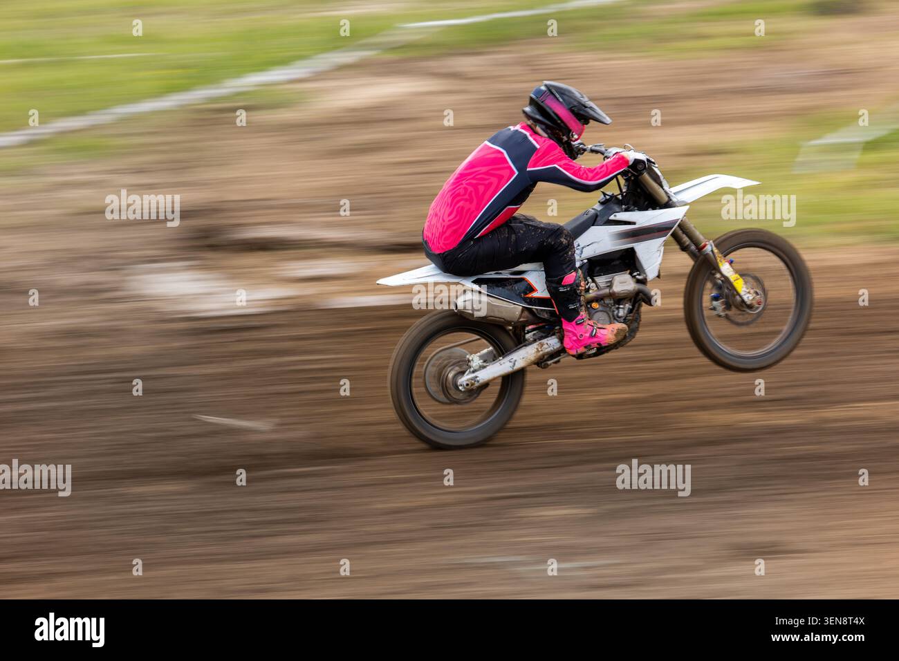 Pilote de motocross dans un équipement de course lumineux vitesse sur piste de terre effet de flou dramatique. Endurance de commande D'accélération de scène D'action dynamique Banque D'Images