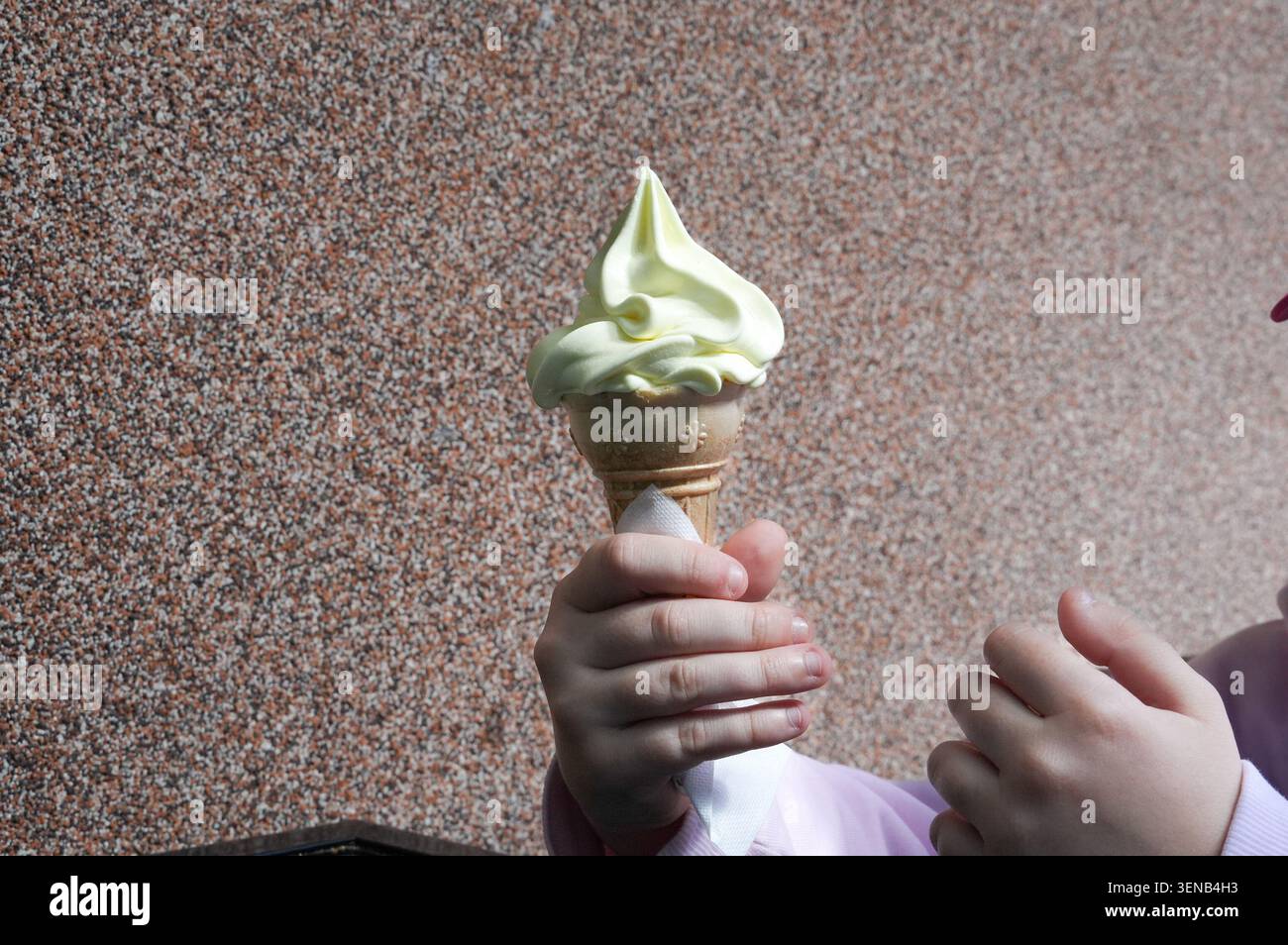 Une main d'enfant tenant une glace en cornet sur un fond marron Banque D'Images