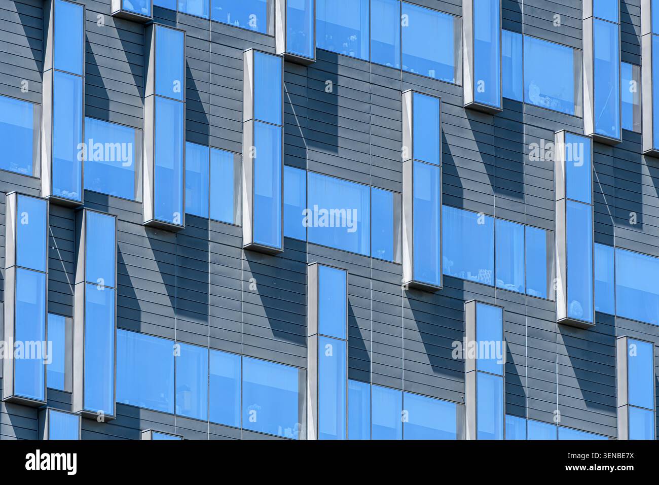 Vue détaillée de la façade de l'hôpital montrant des vitrages teintés en bleu, des panneaux métalliques et des projections de fenêtre angulaires. Banque D'Images