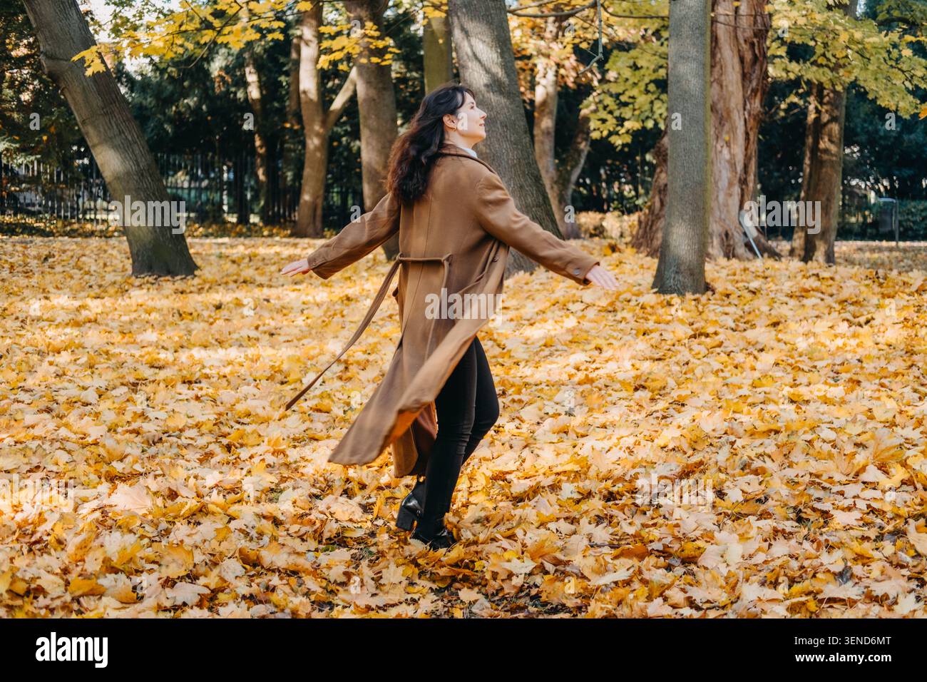 Femme marche à travers le parc rempli de feuilles d'automne tombées tout en regardant en arrière. Vacances à faible empreinte carbone, industrie des loisirs en plein air d'automne Banque D'Images