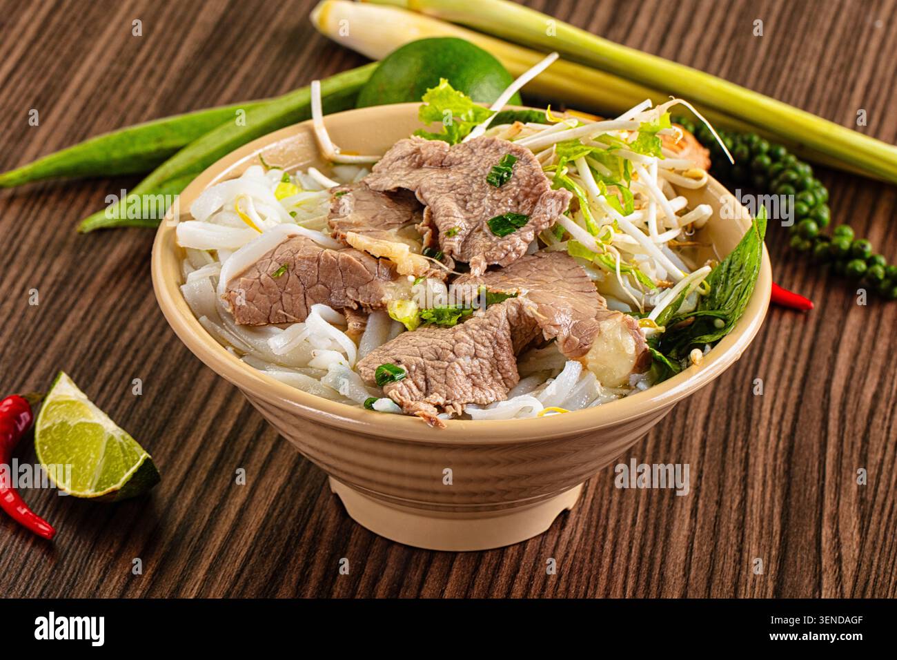 Bol appétissant de soupe traditionnelle vietnamienne de nouilles de bœuf pho, garni d'herbes fraîches, de germes de haricots, de citron vert tranché sur une table en bois rustique Banque D'Images