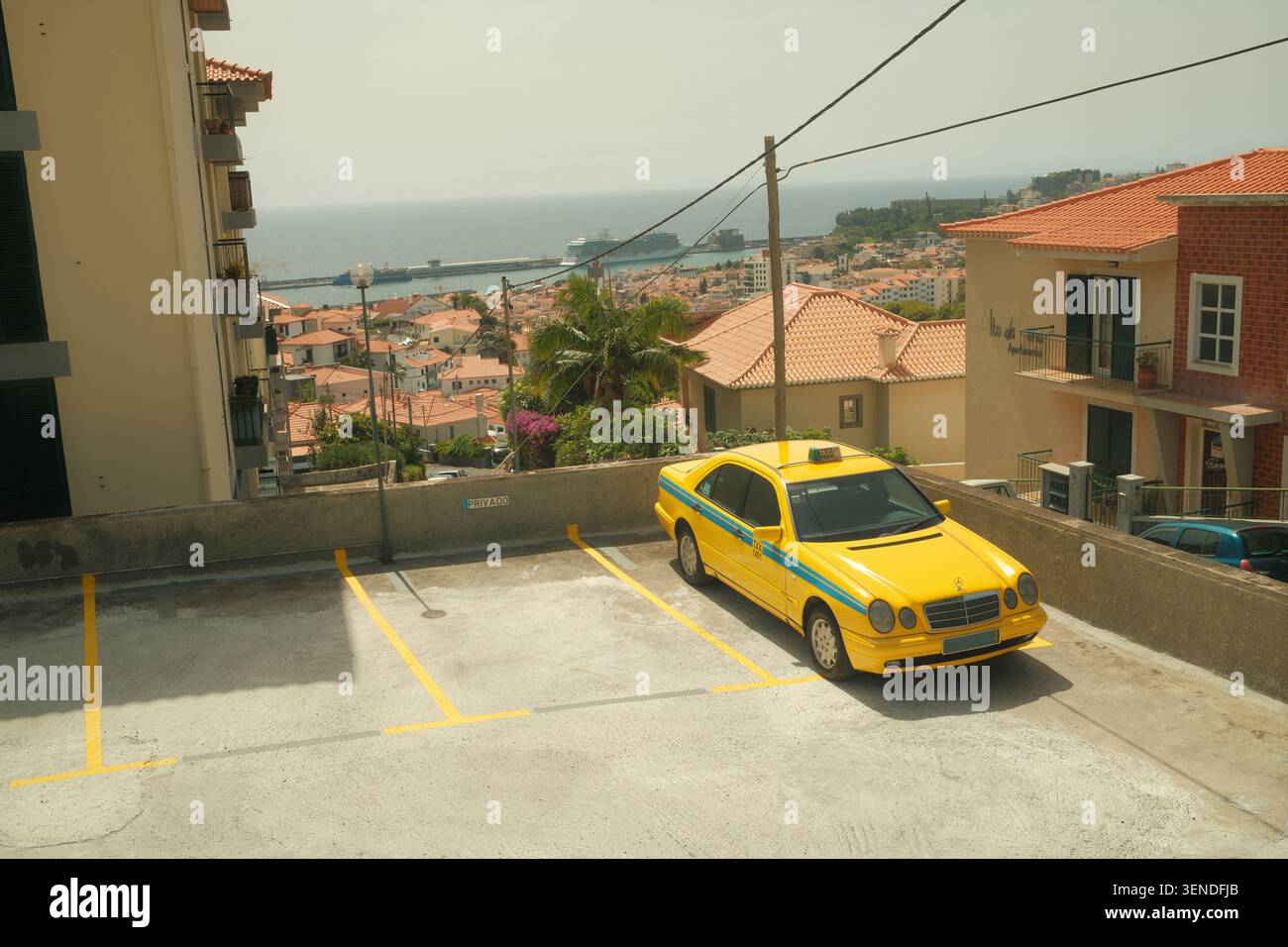 Taxi Mercedes jaune garé à Funchal, Madère, Portugal, avec vue panoramique sur les toits de la ville, le port des bateaux de croisière et l'océan Atlantique Banque D'Images