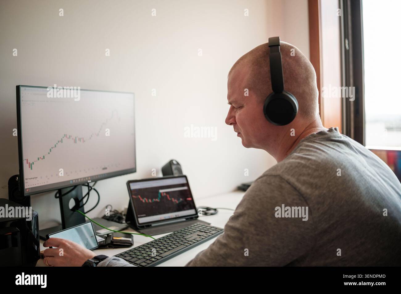 Homme surveillant les graphiques boursiers et les tendances des crypto-monnaies sur ordinateur, tablette et téléphone Banque D'Images