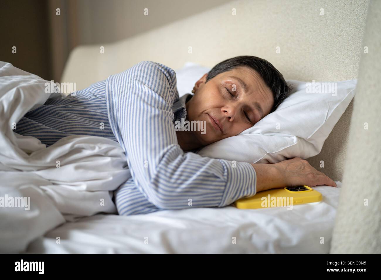Femme senior calme dormant confortablement dans le lit à la maison avec smartphone couché à côté de l'oreiller. Banque D'Images
