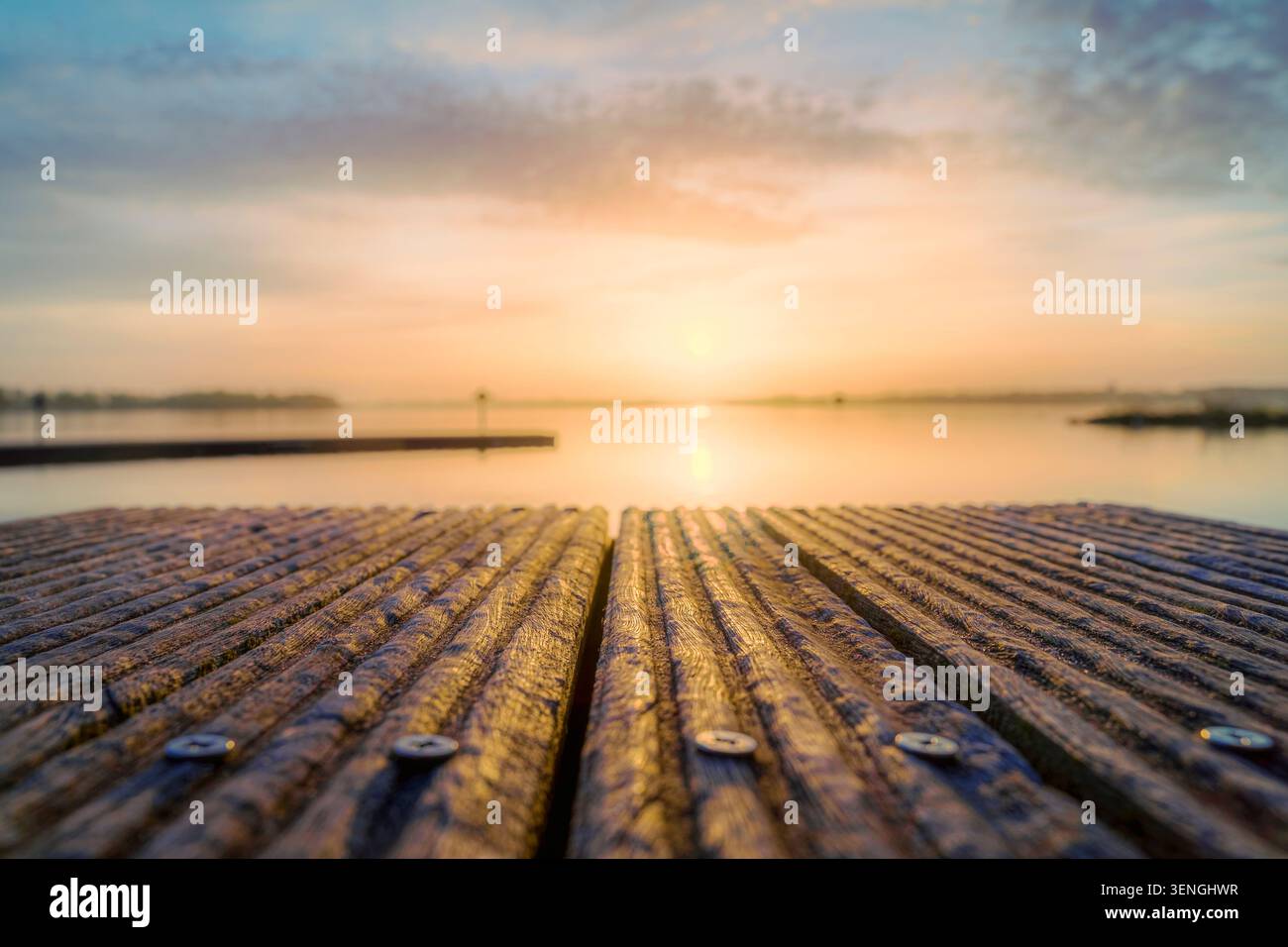 Des planches de bois mènent à un lac serein au lever du soleil, reflétant les teintes douces du ciel. Banque D'Images