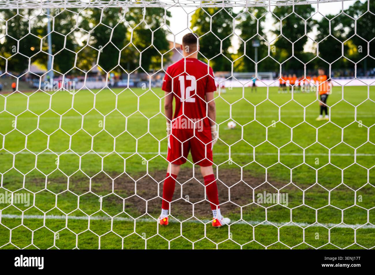Regardez à travers le filet d'un gardien de but de football dans un kit rouge se préparant à défendre un penalty lors d'un match de football. Banque D'Images