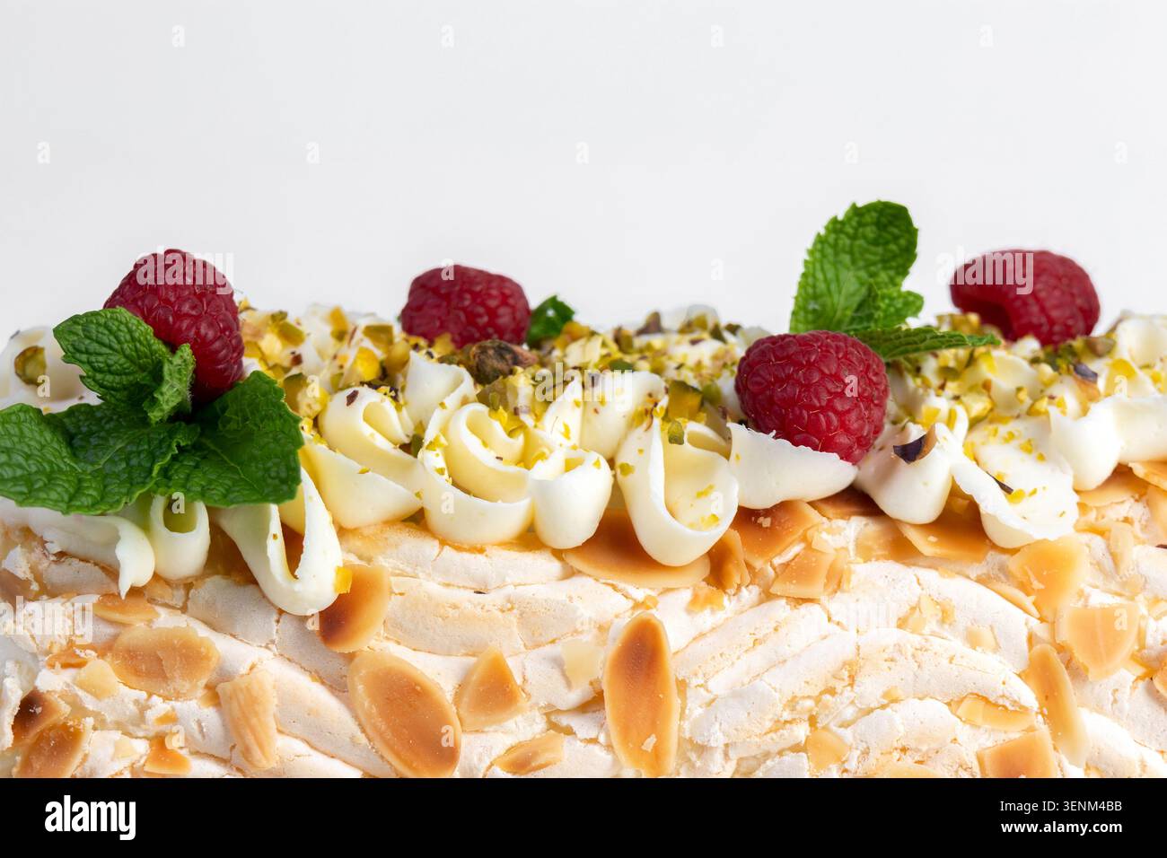 Beau gâteau festif en rouleau de meringue maison avec fromage à la crème, décoré de chips d'amandes et de crumbles de pistaches, de framboises et de feuilles de menthe Banque D'Images