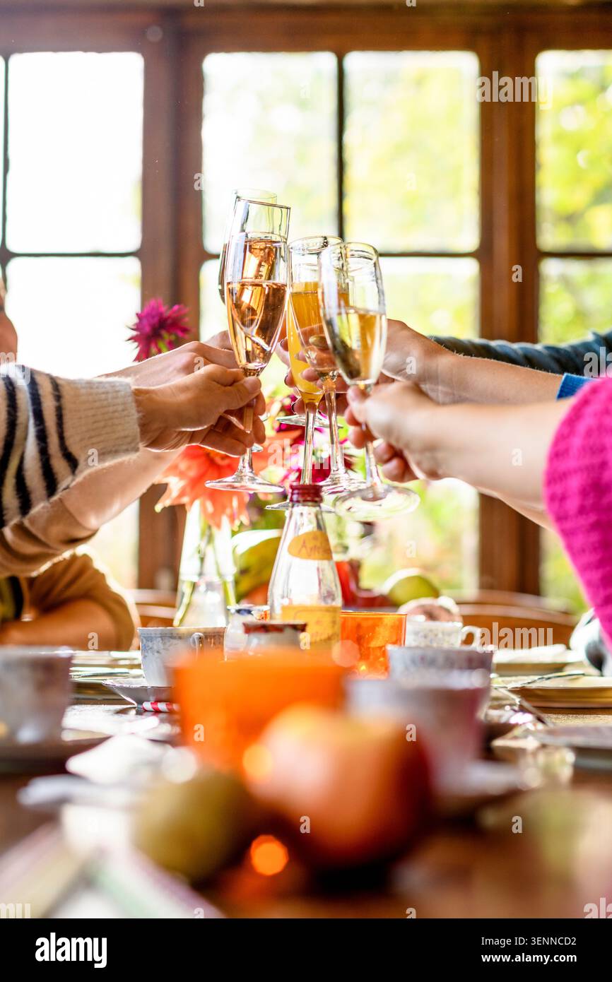 Amis toast avec des verres à champagne à une table de brunch avec des fruits et des fleurs d'automne, lumière naturelle de grandes fenêtres. Banque D'Images