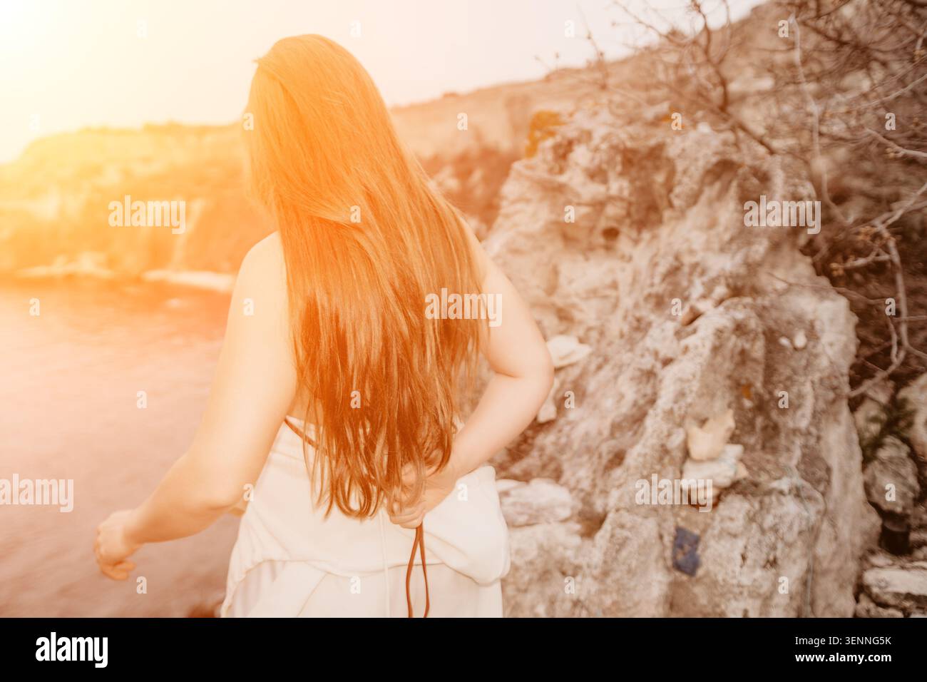 Coucher de soleil de cheveux de femme debout sur la côte rocheuse regardant la mer pendant l'heure dorée Banque D'Images