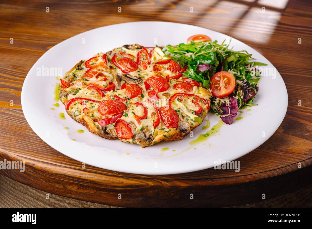Omelette frittata avec tomates cerises et salade fraîche servie sur une assiette blanche dans un café. La scène se déroule dans un café à la lumière du jour. Banque D'Images