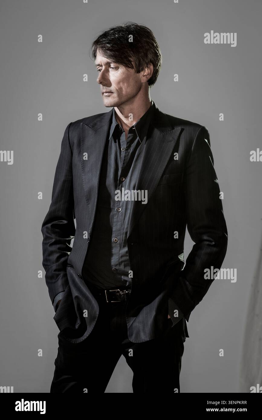 Brett Anderson se tient debout dans un cadre de studio, portant un costume et une chemise. Il regarde bien sur le côté, les mains dans les poches. L'éclairage met en valeur le sien Banque D'Images