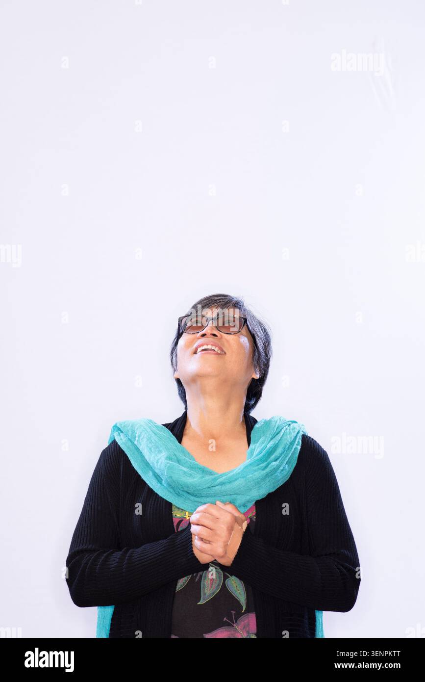 L'écrivain Candy Gourlay se tient debout avec un grand sourire, levant les yeux portant une écharpe vert turquoise et des lunettes de soleil. L'arrière-plan est léger et simple Banque D'Images