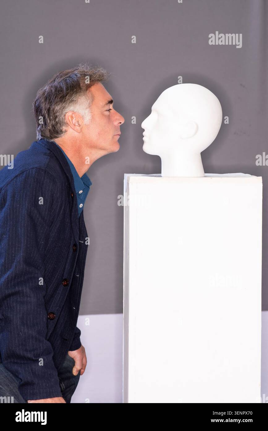L'acteur Greg Wise se penche près d'une tête de mannequin blanche dans un studio. Le paramètre a un arrière-plan simple. Banque D'Images