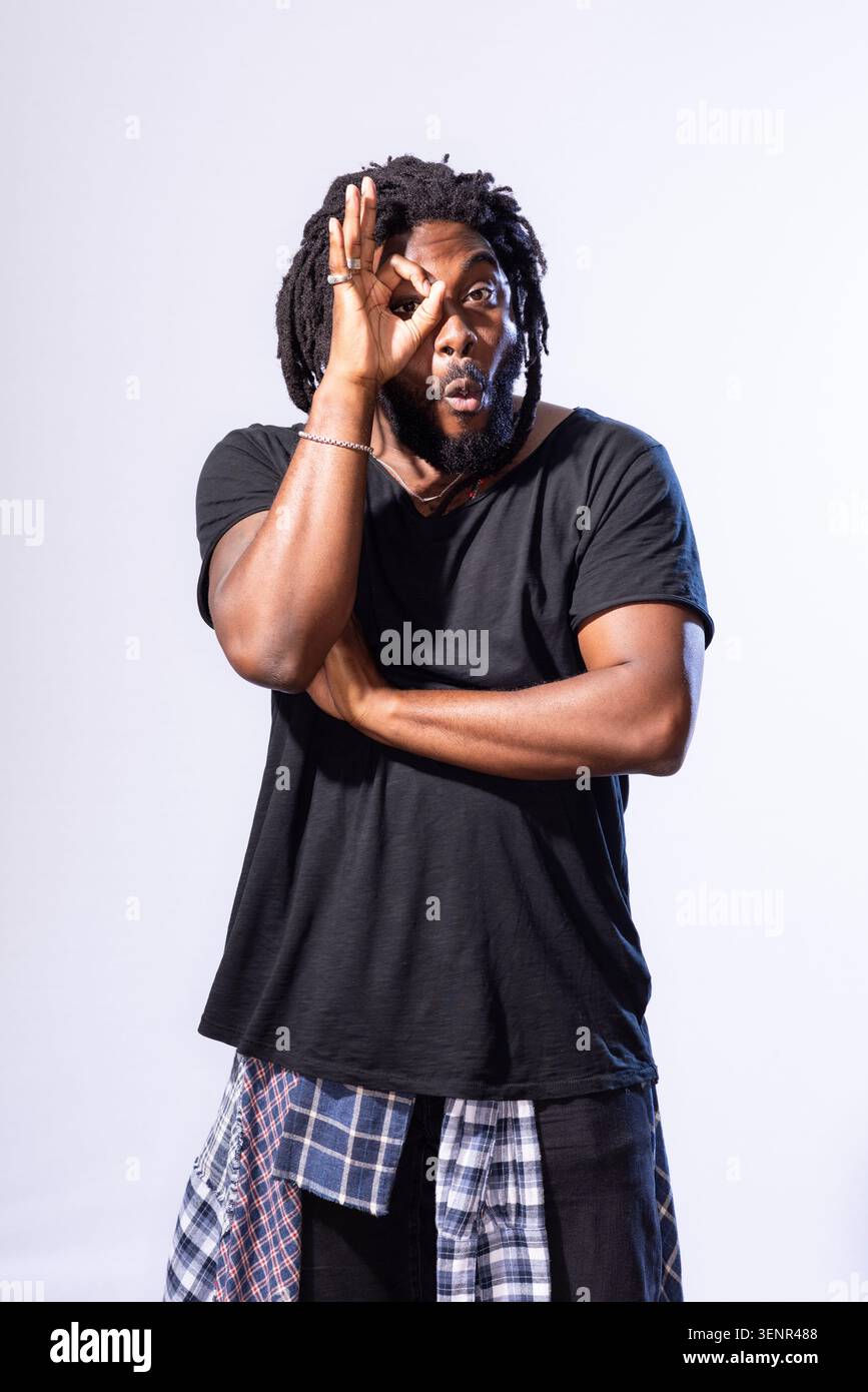 Portrait de Jason Reynolds. Il tient sa main sur son visage et porte une chemise noire et un Jean, une chemise à carreaux nouée autour de sa taille Banque D'Images