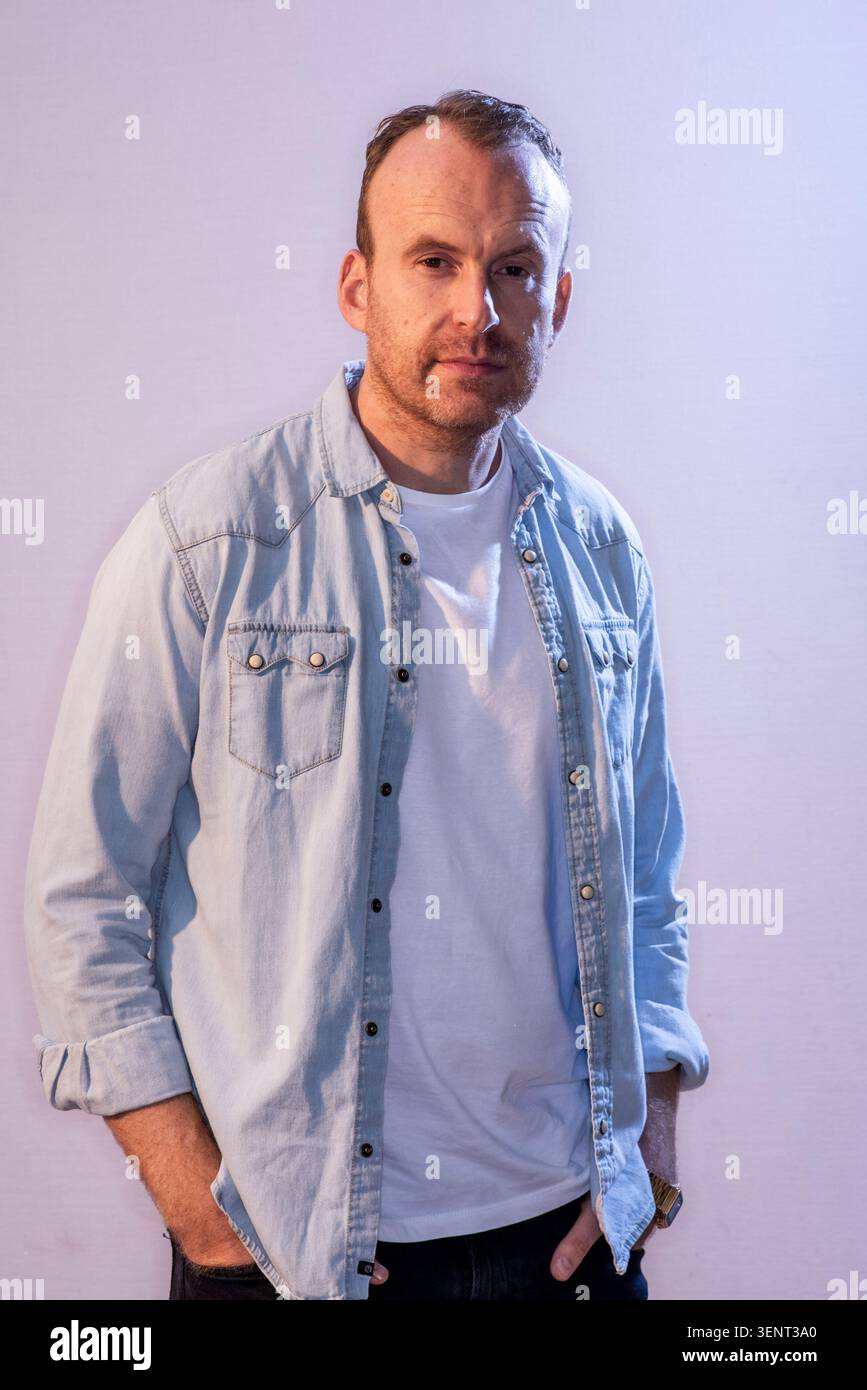 Le scénariste Matt Haig pose pour une photo tout en regardant directement la caméra. Il porte une chemise en denim sur un t-shirt blanc. L'arrière-plan est clair. Banque D'Images