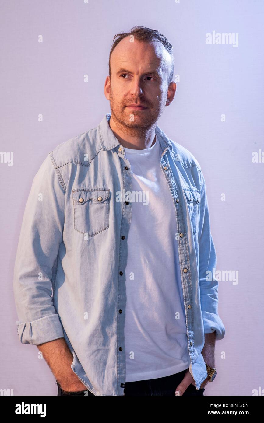 Le scénariste Matt Haig pose pour une photo tout en regardant directement la caméra. Il porte une chemise en denim sur un t-shirt blanc. L'arrière-plan est clair. Banque D'Images