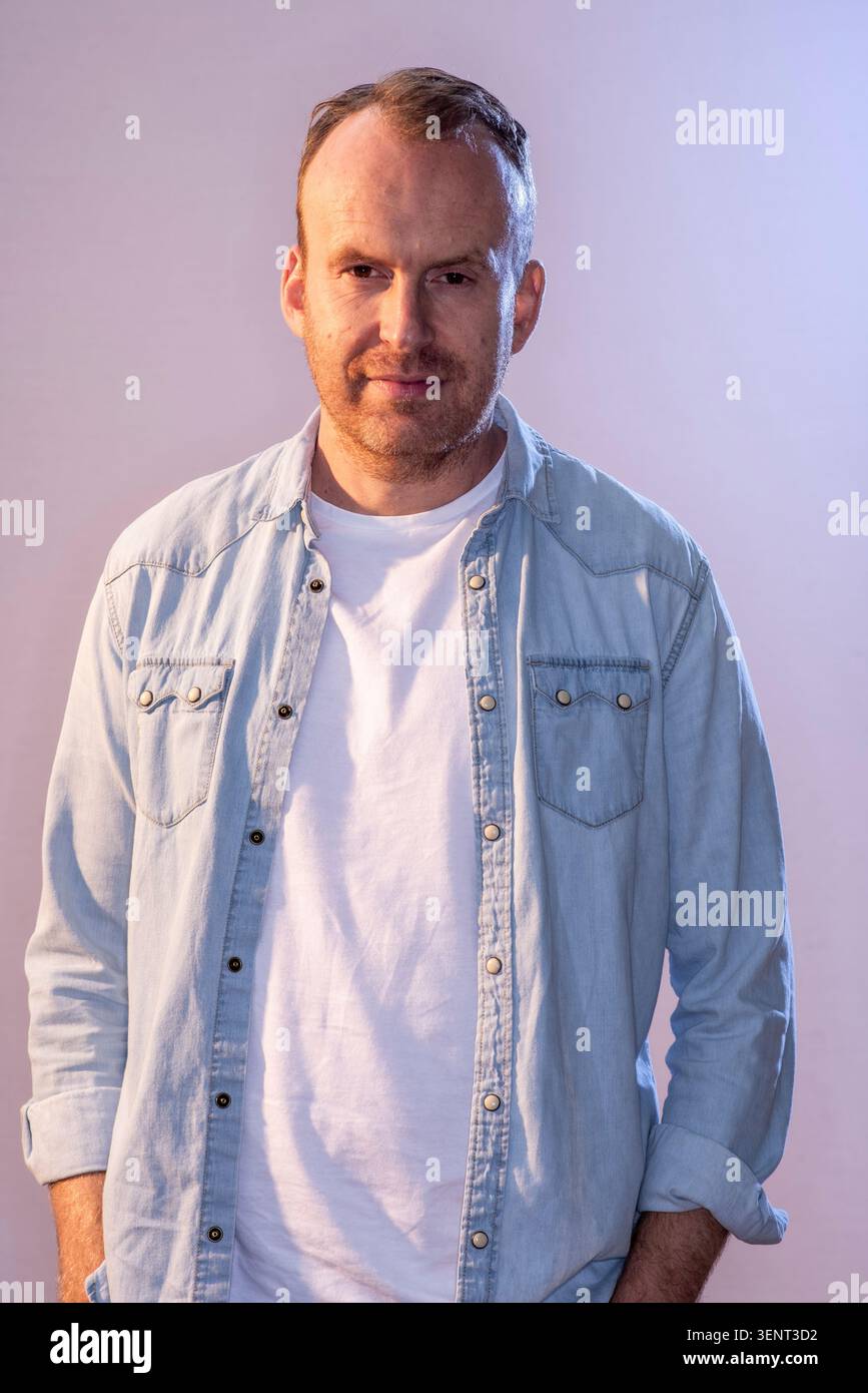 Le scénariste Matt Haig pose pour une photo tout en regardant directement la caméra. Il porte une chemise en denim sur un t-shirt blanc. L'arrière-plan est clair. Banque D'Images