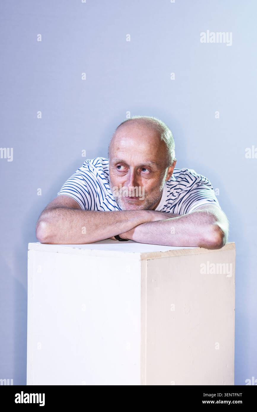 L'artiste de bande dessinée britannique Warren Pleece se penche en avant, les bras reposant sur un bloc blanc. Il semble calme et concentré en regardant la caméra. Banque D'Images