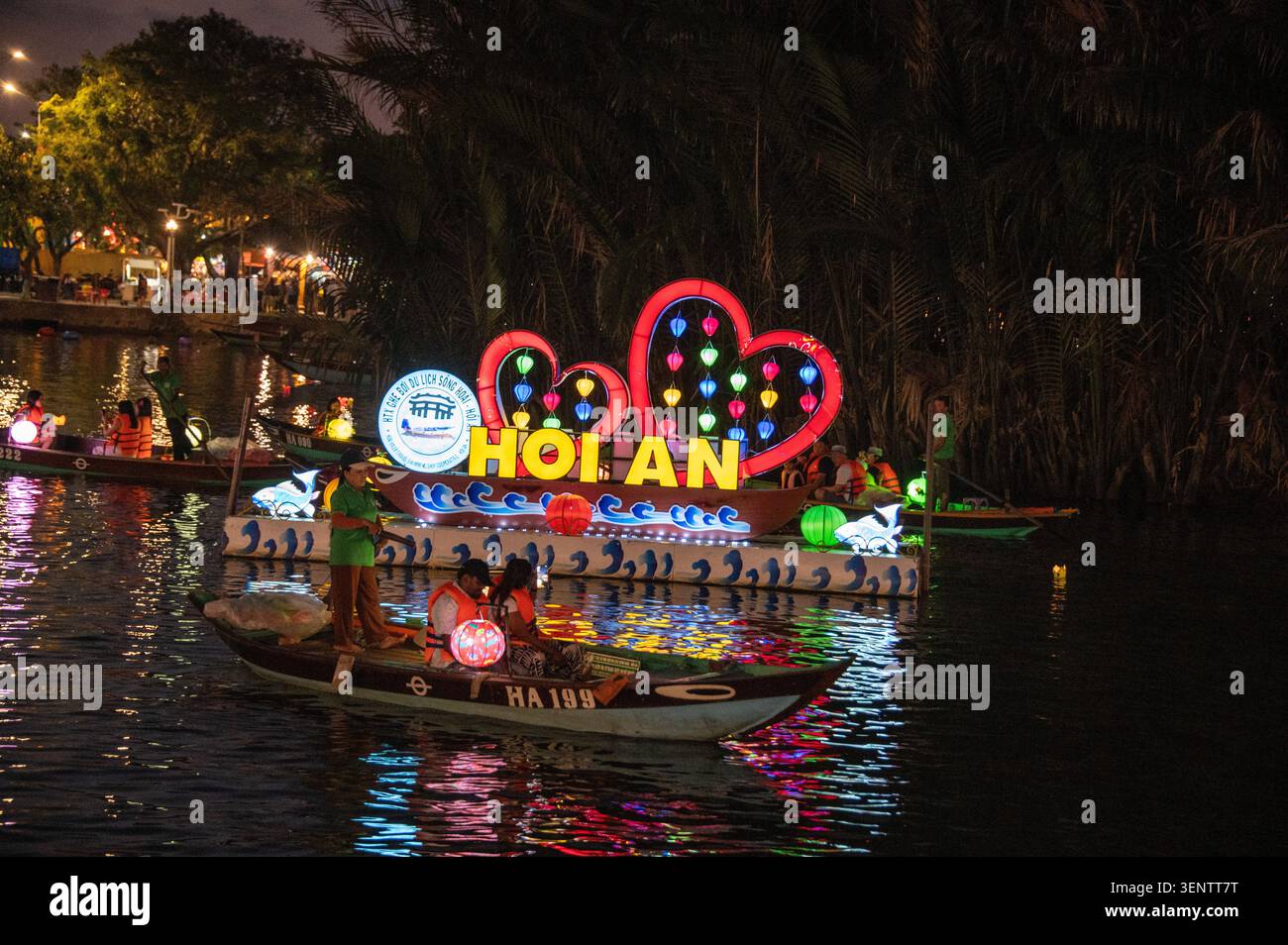 Les bateaux flottent devant une île flottante éclairée sur la rivière Thu bon à Hoi an. Hoi an est célèbre pour sa flottille nocturne de sampans (bateaux à fond plat) avec Banque D'Images