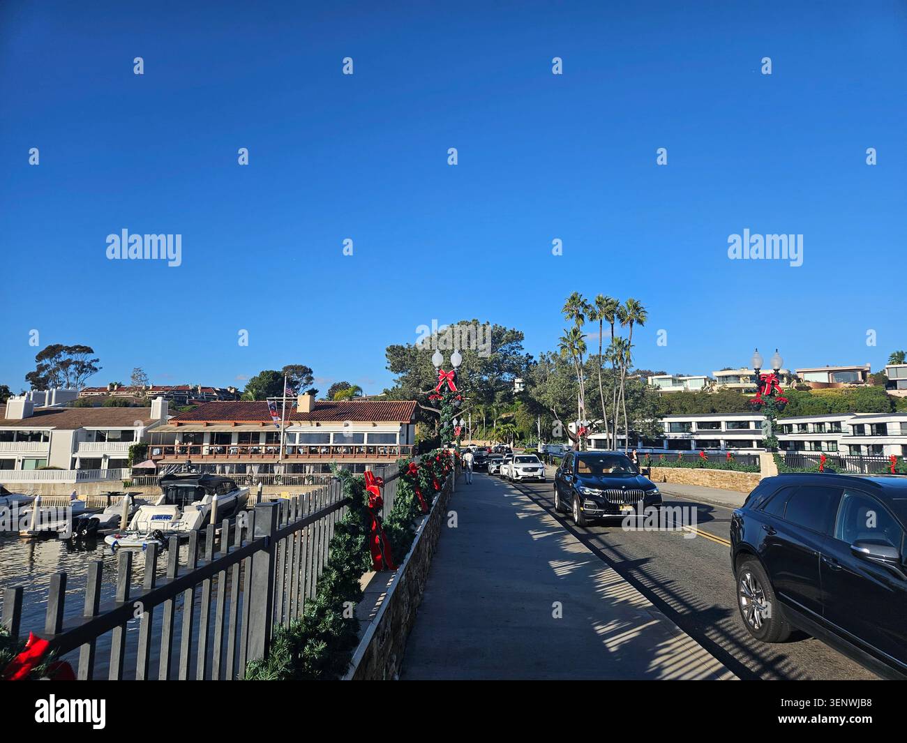 Scène portuaire calme à Balboa Island à Newport Beach, Californie, avec des bateaux amarrés, des maisons en bord de mer, des palmiers, reflets du soleil sur l'eau, et a Banque D'Images