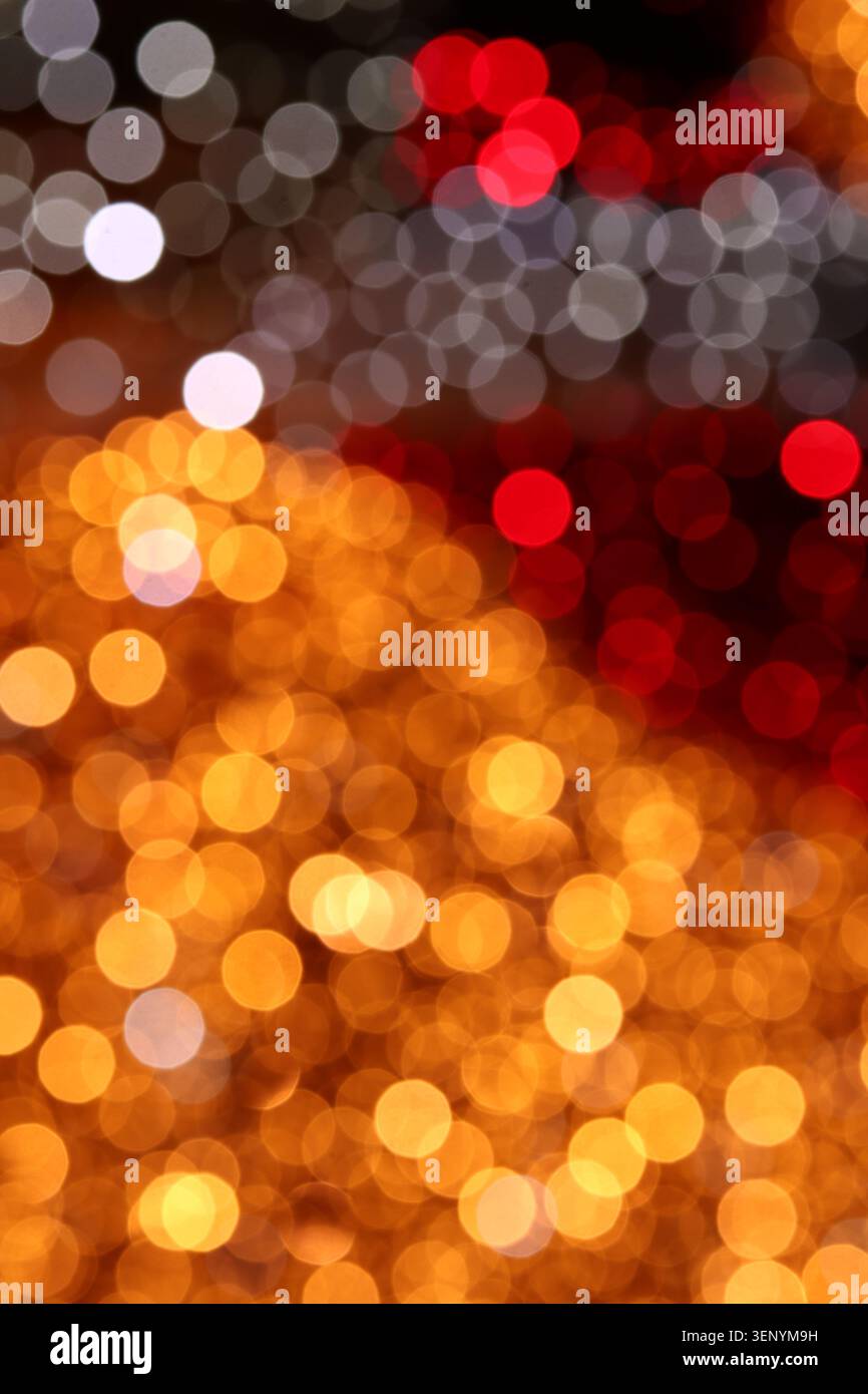Plan de bokeh vertical évoquant une rue nocturne animée, avec des lumières orangées dorées en dessous qui s'estompent en gris froid et rouge au-dessus. Forte illusion de profondeur, perfec Banque D'Images