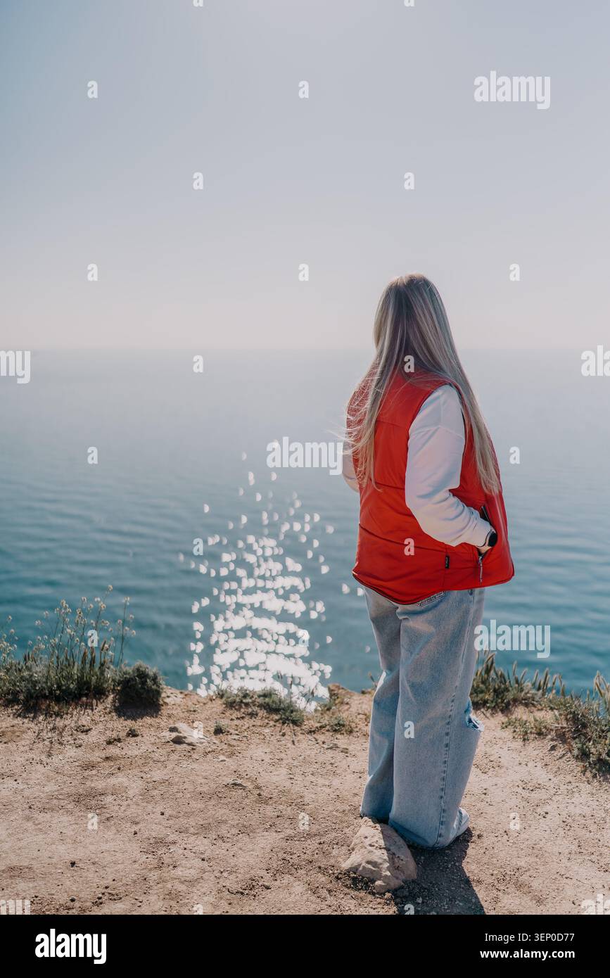 Femme falaise océan. Jeune femme debout sur un bord de falaise surplombant la mer bleue calme sous un ciel clair avec espace de copie Banque D'Images