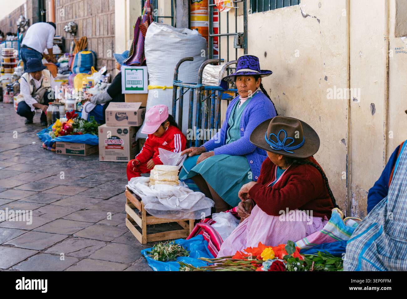Cusco, Pérou - 23 mars 2025 : des vendeurs de rue en vêtements andins traditionnels sont assis le long d'un trottoir à l'extérieur du marché San Pedro à Cusco Banque D'Images