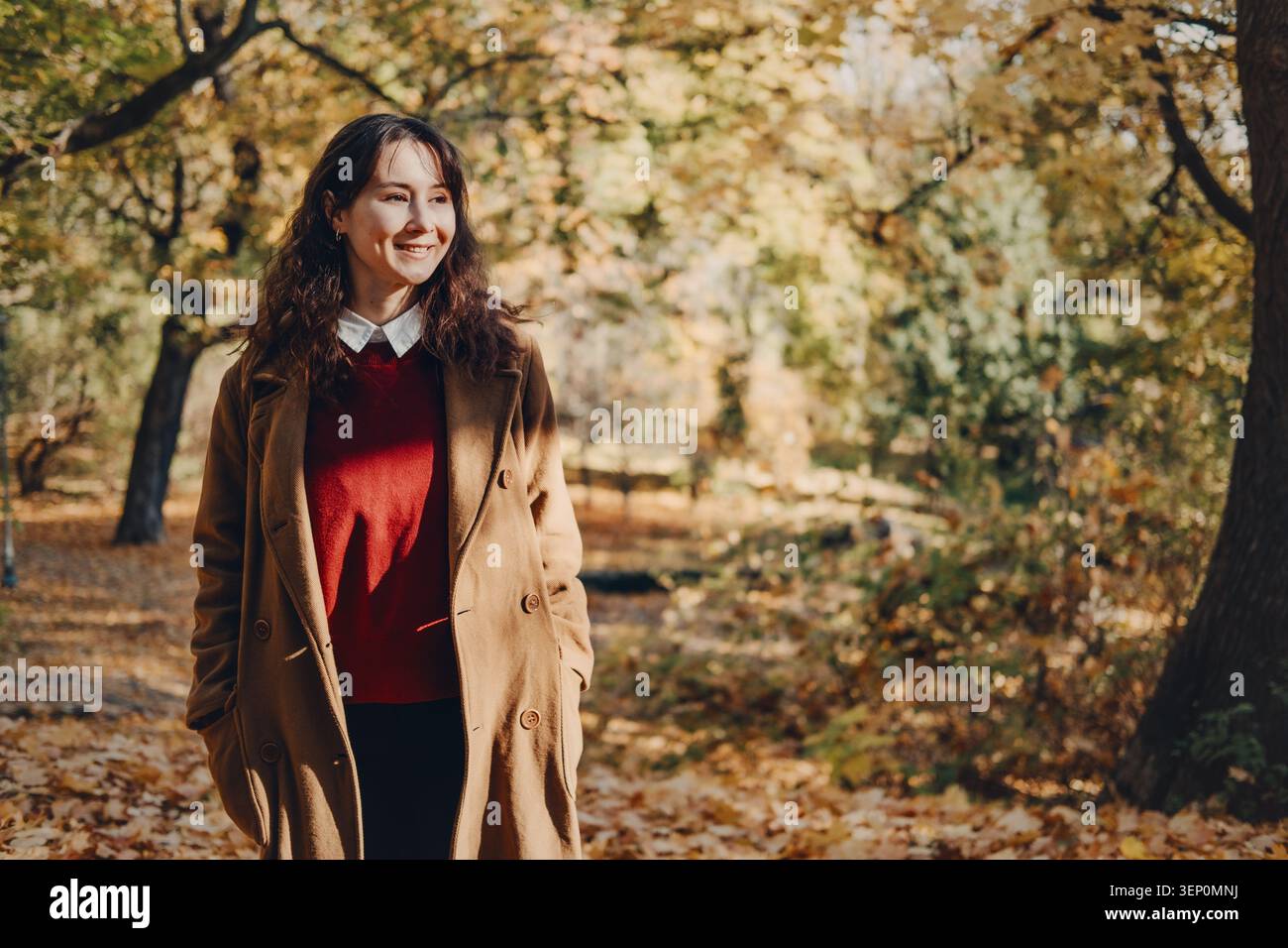 Personne se tient souriant dans le parc ensoleillé rempli d'arbres d'automne jaunes. Promenade nature de soulagement du stress, activité de détox numérique en plein air, équilibre émotionnel Banque D'Images