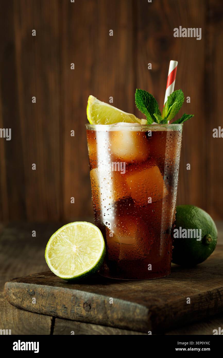 Cocktail cuba libre rafraîchissant avec cola, rhum, citron vert et menthe, boisson fraîche avec glaçons sur une table en bois rustique Banque D'Images