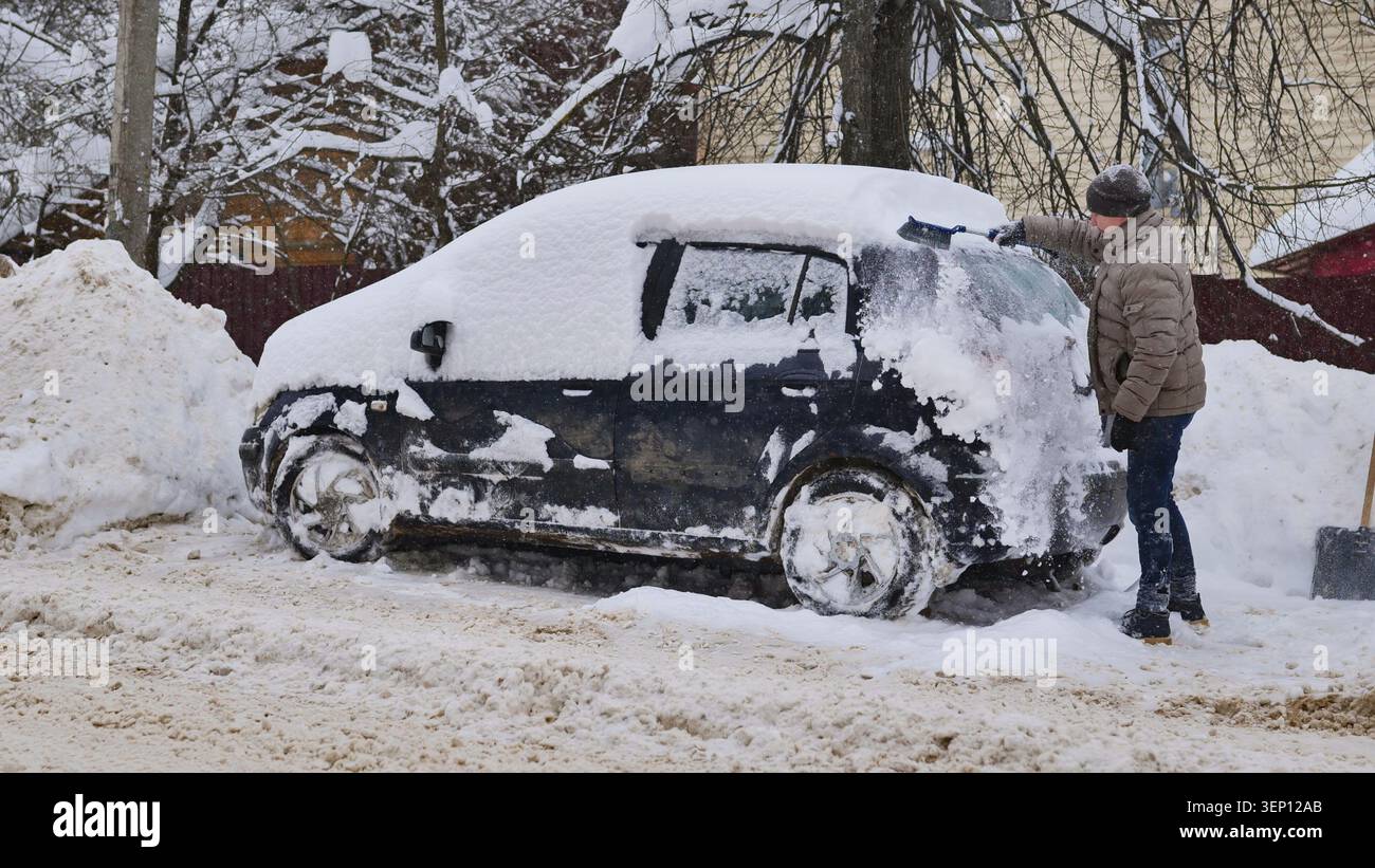 Homme grattant la neige de la voiture dans des conditions hivernales difficiles pendant un blizzard Banque D'Images