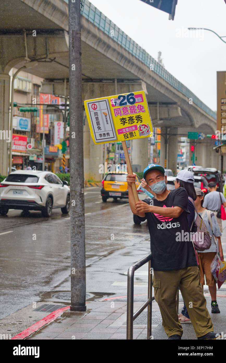 Taipei, Taiwan - 19 juillet 2025 : volontaire en masque tient un panneau jaune appelant à rappeler le législateur Neihu-Nangang Li Yen-hsiu sur la rue pluvieuse de Taipei. Banque D'Images