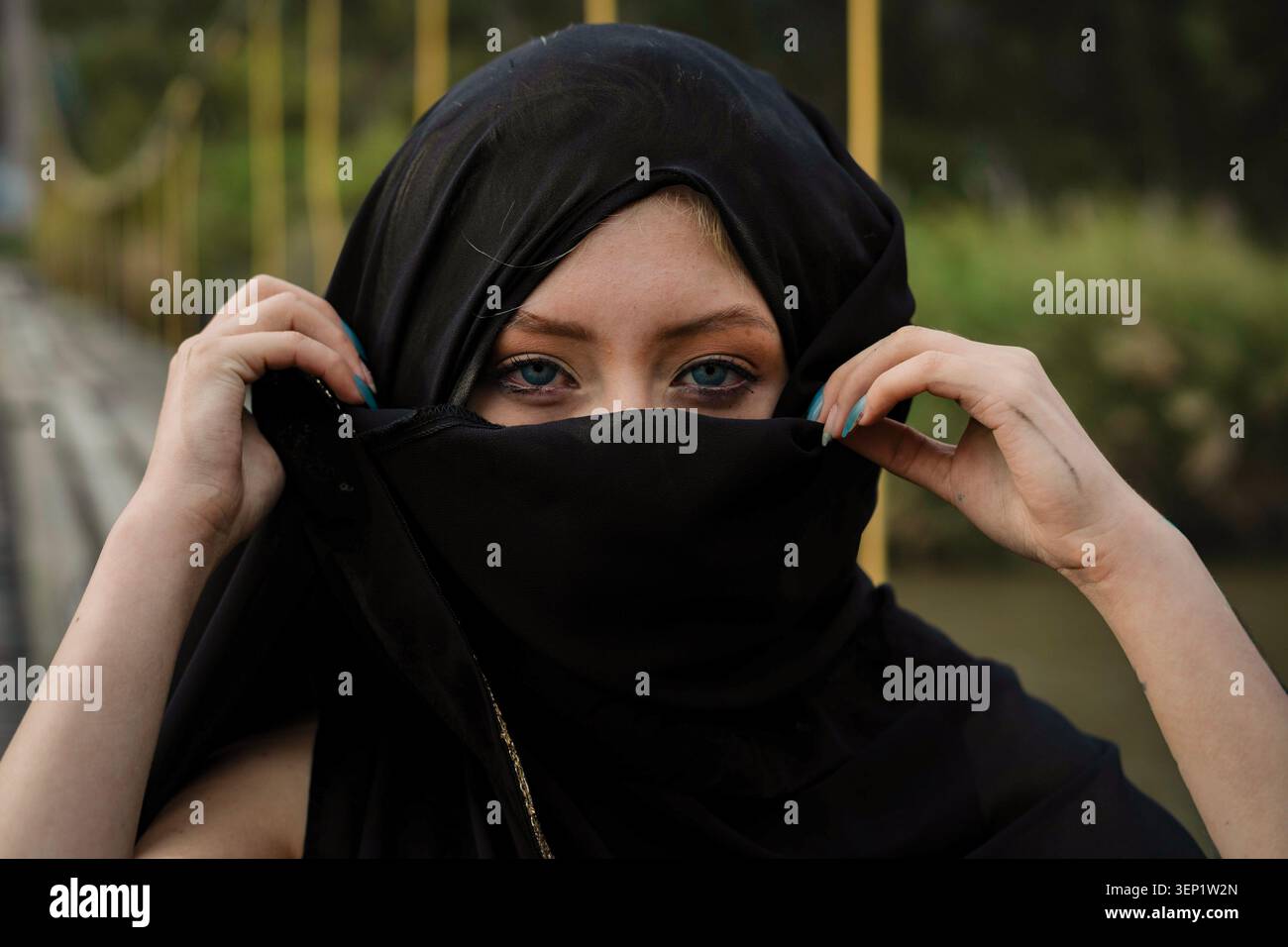 Femme aux yeux bleus frappante regardant sous un niqab noir, visage et tête partiellement couverts, portrait serein et contemplatif véhiculant une identité culturelle Banque D'Images