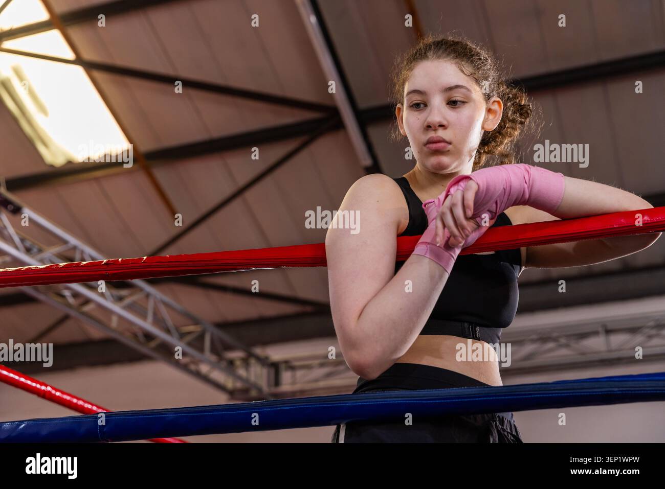 Boxeur adolescente se penchant sur une corde rouge au gymnase, portant un soutien-gorge de sport noir, enveloppant rose Banque D'Images