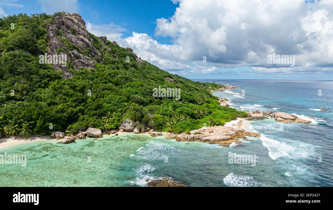 Formations rocheuses massives couvertes de verdure, entourées d'eaux turquoises claires sous un ciel bleu. Seychelles, la Digue. Banque D'Images