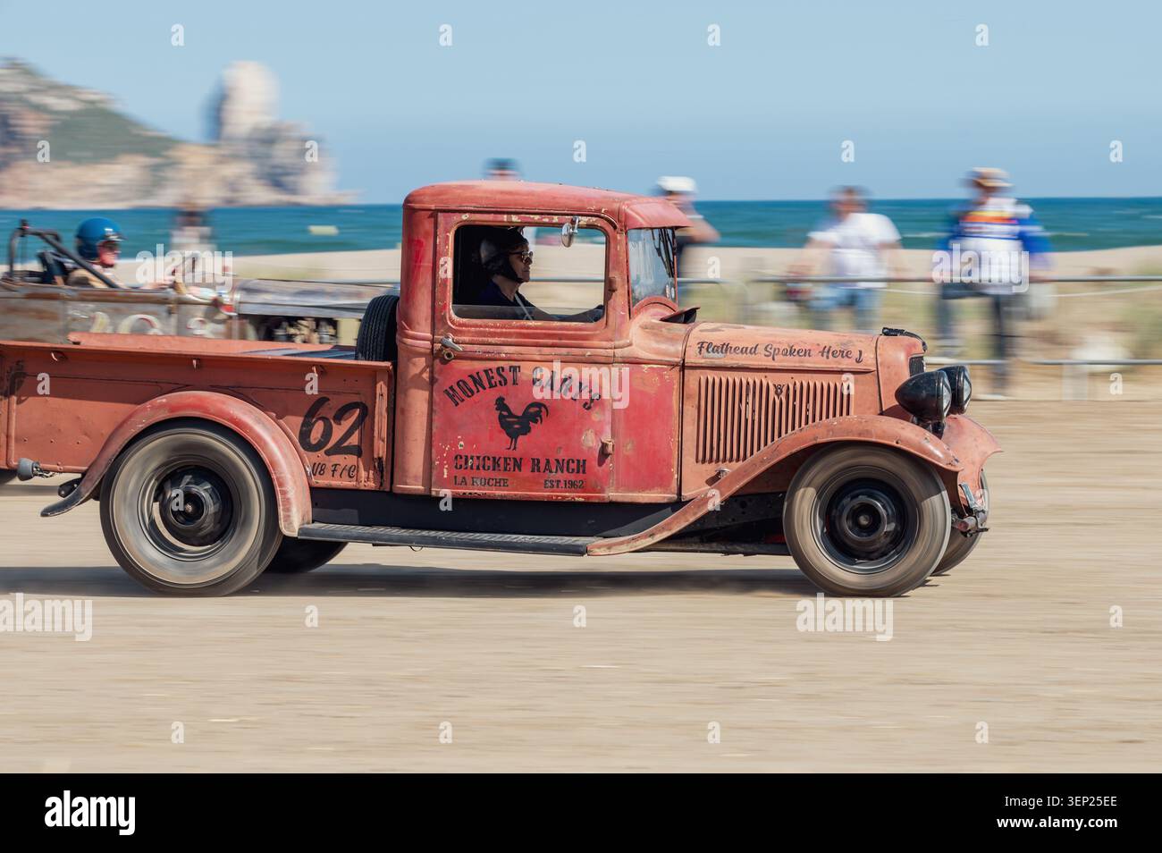 Vue latérale panoramique d'une camionnette rouge vintage Ford modèle 46 faisant la course d'un autre véhicule classique sur une plage de sable fin lors d'une traînée traditionnelle Banque D'Images
