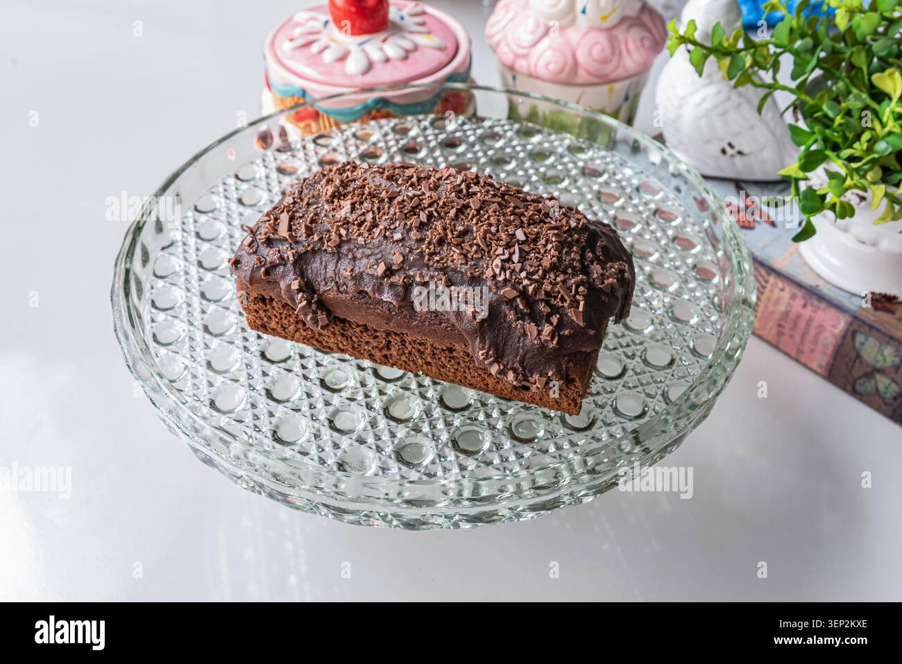 Gâteau au chocolat avec ganache et copeaux de chocolat sur plaque de cristal. Gâteau aux couleurs riches et sombres contre un blanc doux, adapté aux menus de boulangerie ou indu Banque D'Images