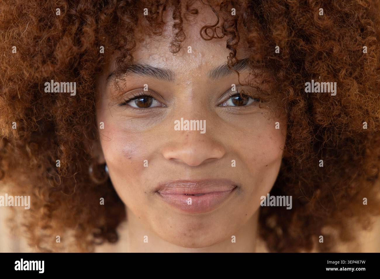 Regardant directement la caméra, femme au milieu des années 20 montrant des cheveux bouclés, brillant à lèvres, boucle d'oreille en studio Banque D'Images