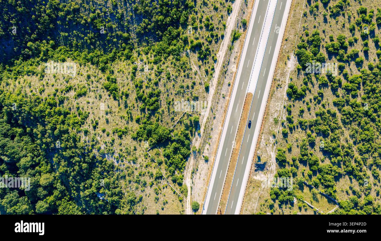 Vue verticale par drone d'une autoroute à plusieurs voies traversant un terrain accidenté, mettant en évidence les réseaux de transport et l'ingénierie routière moderne Banque D'Images