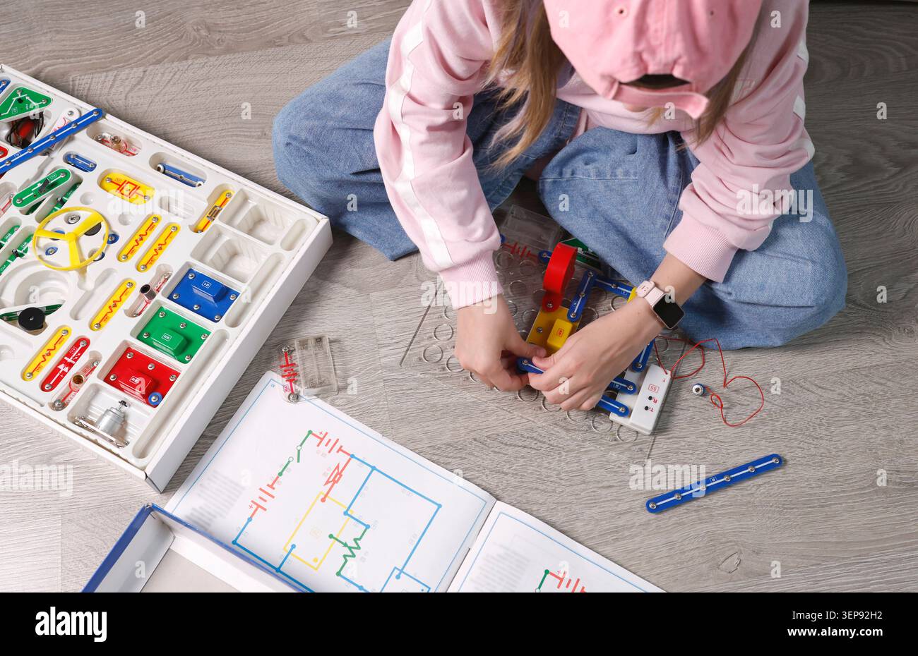 Enfant portant un capuchon rose assemblant des blocs de circuit électronique sur la plaque de base de la grille. Activité pédagogique de laboratoire STEM pour manuel de sciences physiques Banque D'Images