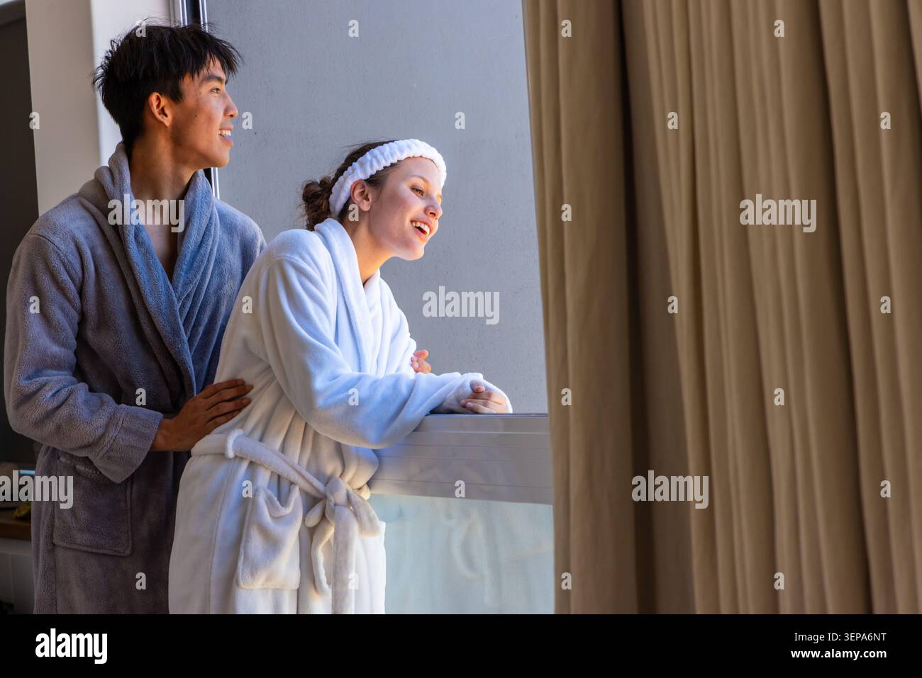 Couple debout à la balustrade en verre dans la suite de l'hôtel, femme penchée, homme tenant la taille, serre-tête de robes Banque D'Images